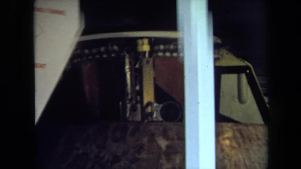 Close 1970 California frame of a brown parade float section with metallic top hardware partly obscured by a pale post.
