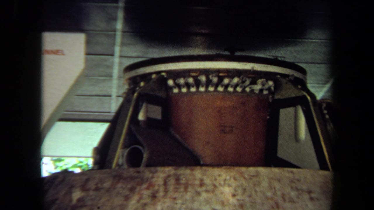 Closer 8mm view of the spacecraft module inside a California exhibit, showing upper fittings and a weathered exterior.