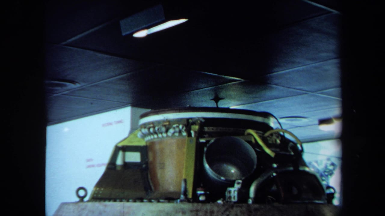 1970 California 8mm frame with industrial machinery, yellow-green supports and a round black housing in a marked docking tunnel area.