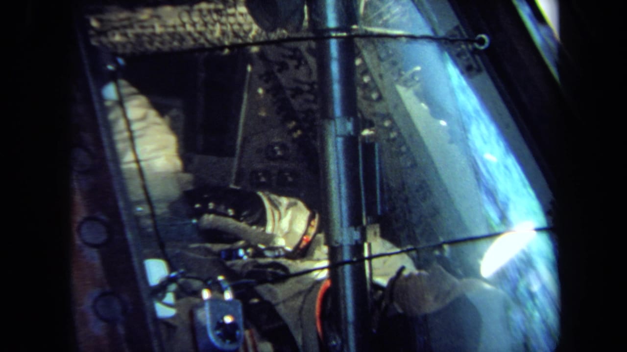 1970 California 8mm frame showing the cockpit-like interior with a suited occupant, gloved hand, window reflections, and metal hardware.