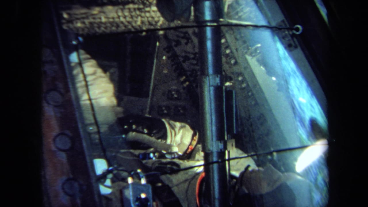 Similar view of the suited figure inside the spacecraft-like display with blue glass reflection.