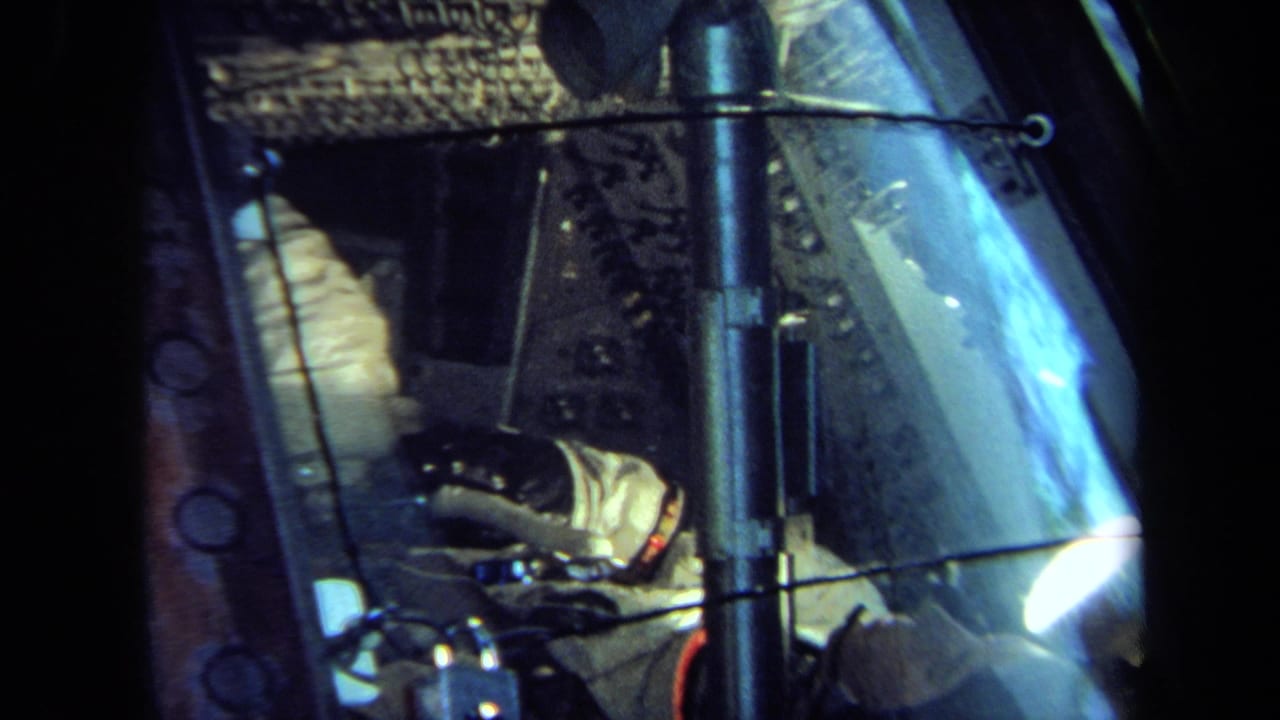 A 1970 California home-movie frame shows the suited figure beside controls and wiring inside a spacecraft-style display.