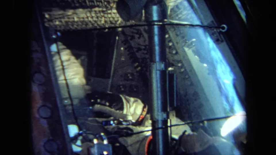 A 1970 California home-movie frame shows the suited figure beside controls and wiring inside a spacecraft-style display.