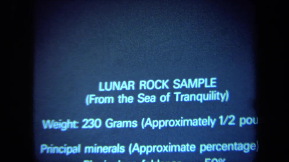 1970 California 8mm frame showing a blue projected slide about a lunar rock sample from the Sea of Tranquility, with lower text cropped.