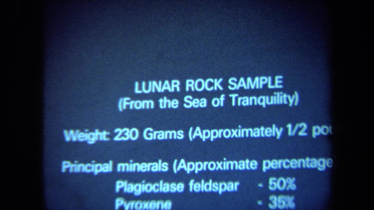 Blue 8mm frame from California in 1970 showing projected text about a Sea of Tranquility lunar rock sample and its mineral makeup.