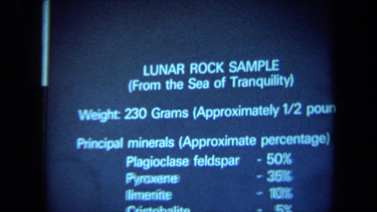 Soft blue 8mm frame showing a projected Sea of Tranquility lunar rock sample slide with weight and mineral details visible.