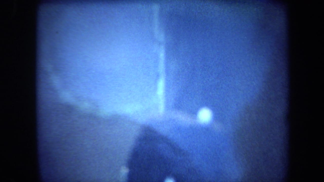 Soft 8mm frame of the blue display at closer range, with a bright reflection and indistinct rock-like texture.