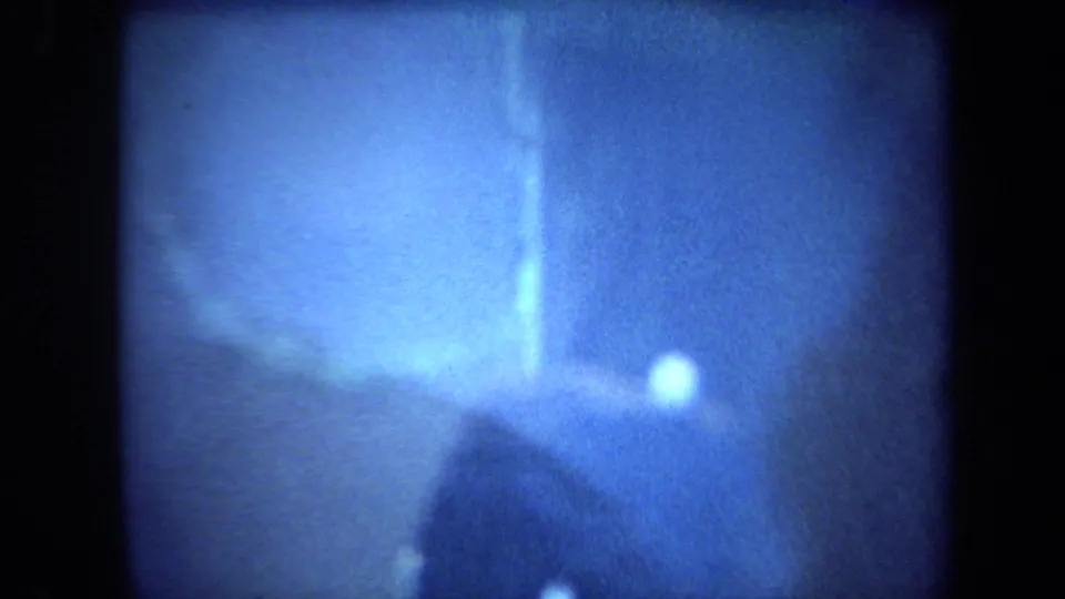 Soft 8mm frame of the blue display at closer range, with a bright reflection and indistinct rock-like texture.