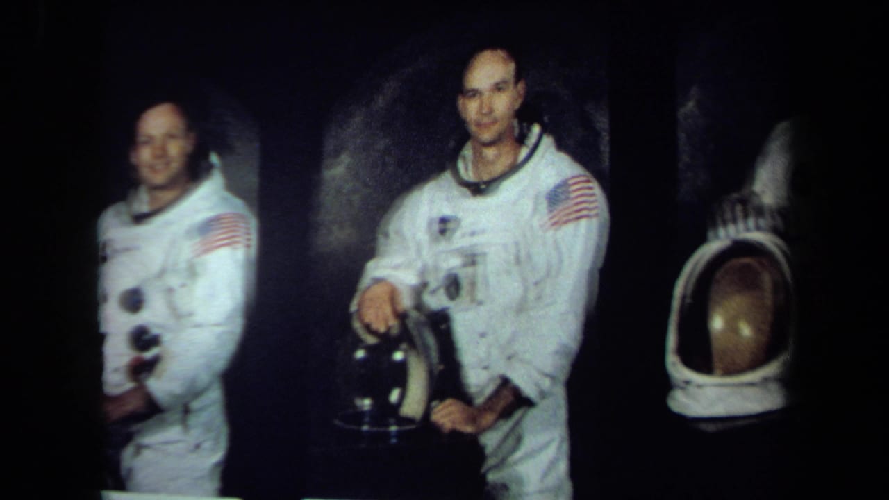 Multiple astronauts in white spacesuits stand with helmets in a dark scene.