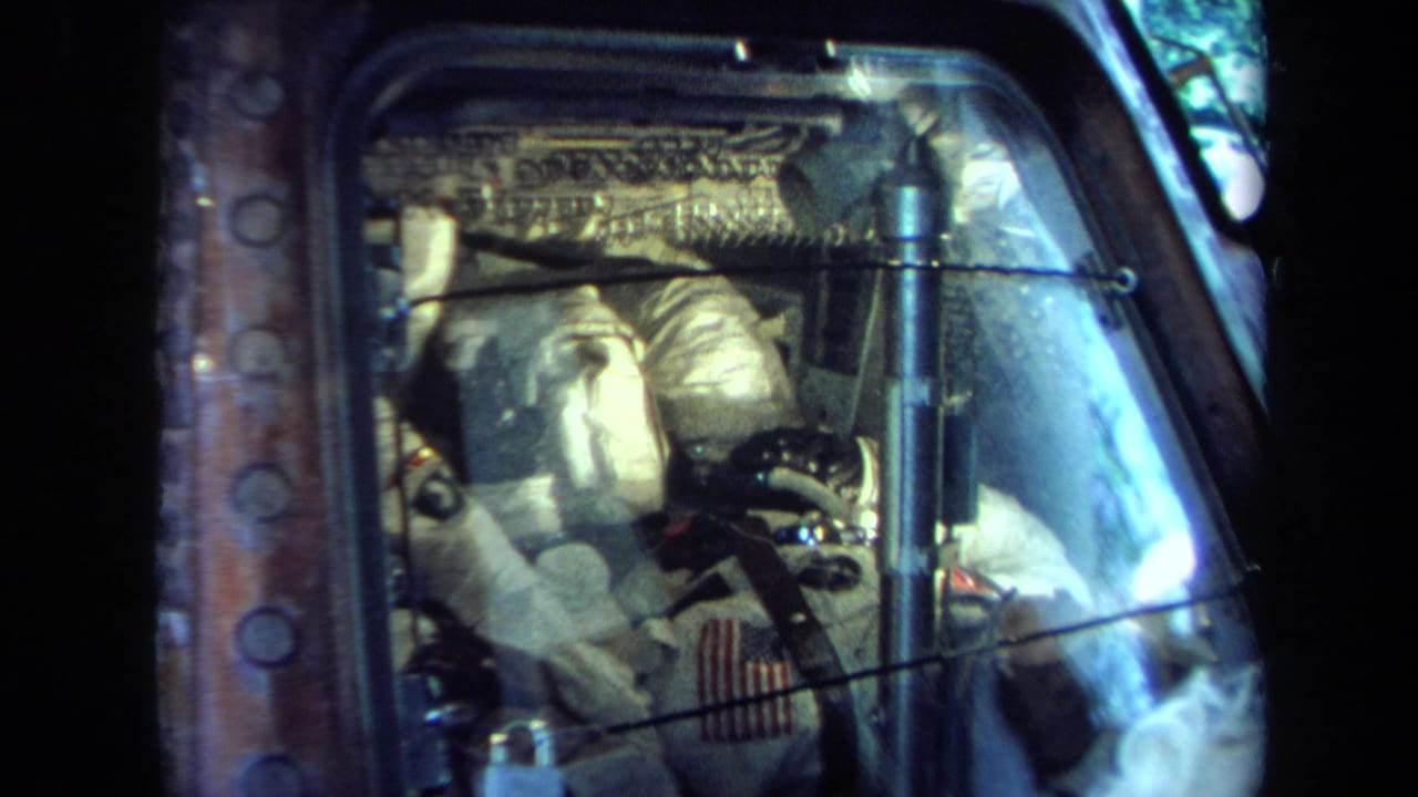 Reflective view into a spacecraft cockpit display with suited astronauts seated among analog panels, wiring, and glass glare.
