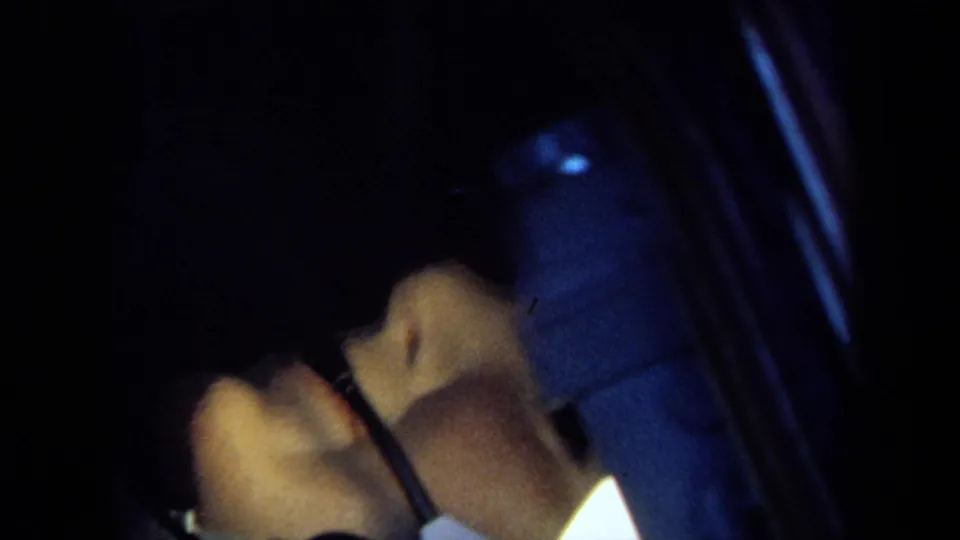 A close, dark 8mm view shows the astronaut figure's raised hands or equipment adjustment inside the cramped capsule space.