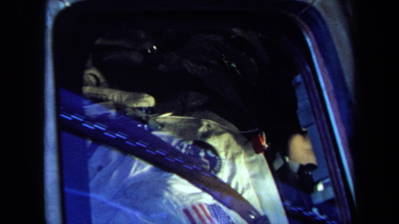 Astronaut figure in a white suit seen through a dark spacecraft window.