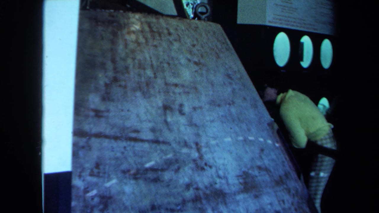 Final frame shows the concrete-like slab beside the dark bus or vehicle, with a person in yellow still partly visible at the right.
