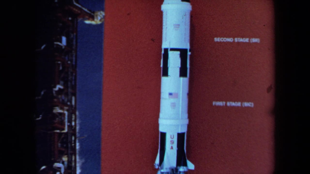 1970 California 8mm frame showing a white NASA-style rocket model against a red stage-labeled display panel.