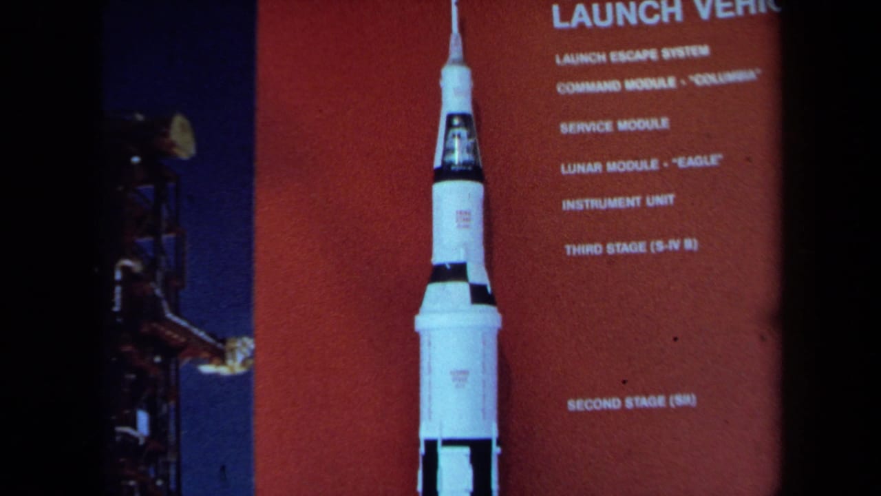 A 1970 California home-movie frame shows the rocket display and launch-vehicle labels, with a partial visitor figure near the edge.