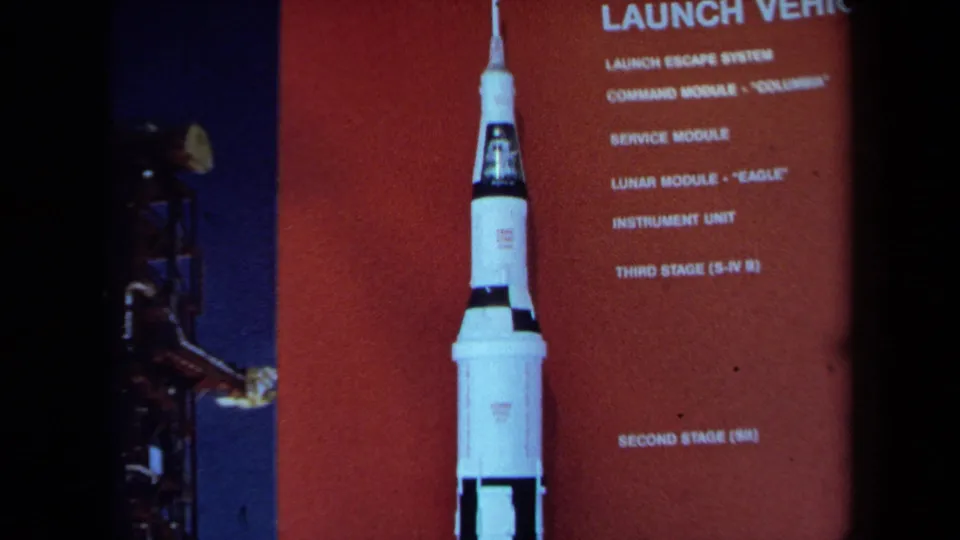 A 1970 California home-movie frame shows the rocket display and launch-vehicle labels, with a partial visitor figure near the edge.