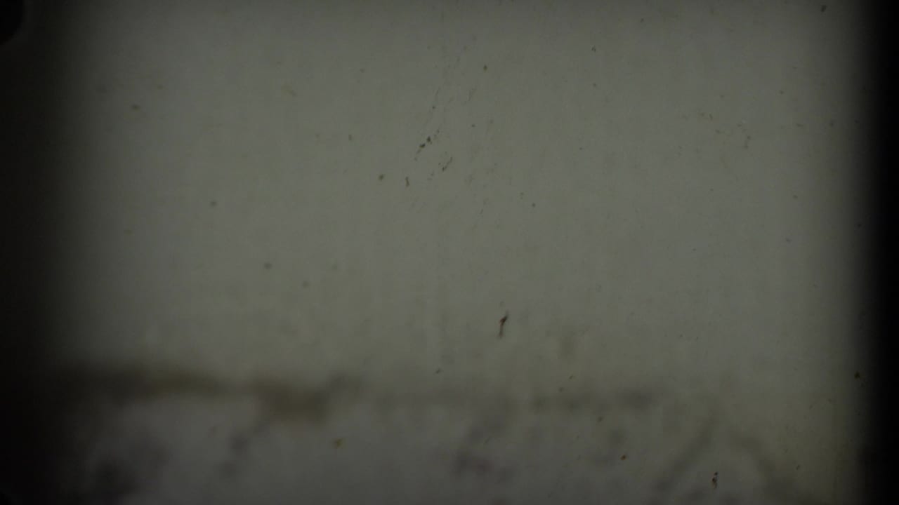 A dark 8mm frame shifts away from the rocket display to a dim, soft-focused sign or pale surface, with heavy vignette at the edges.