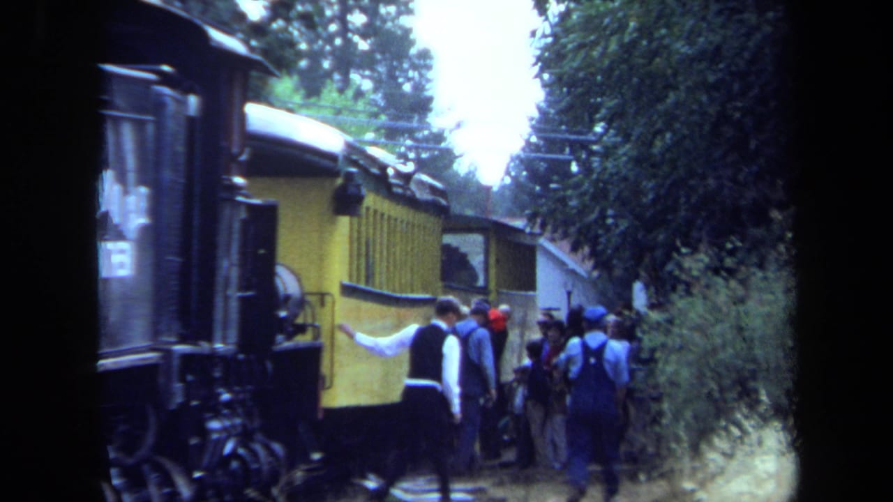 Passengers in casual 1970s clothing move around a yellow railcar during a wooded train stop in California.