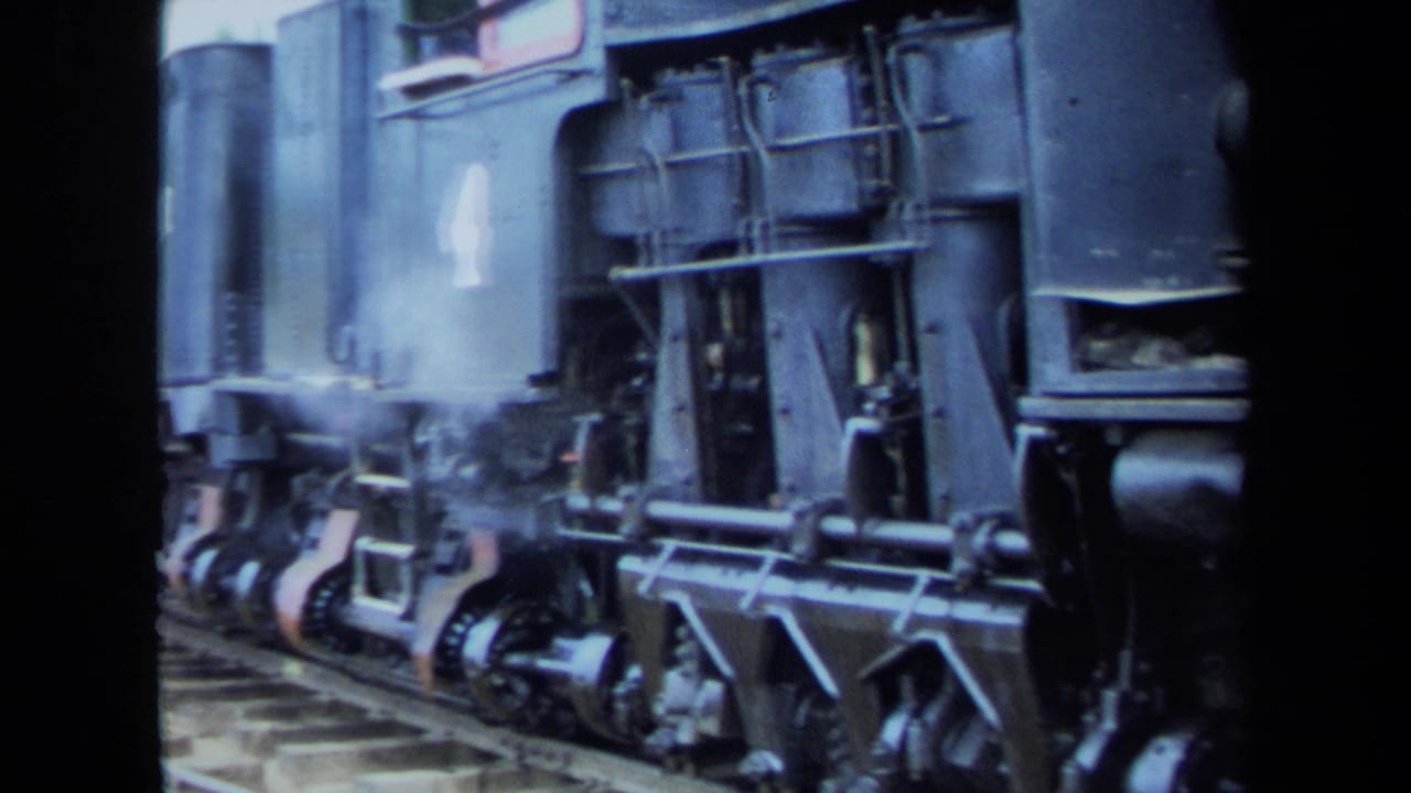 1970 8mm California home-movie frame showing a close side view of a steam locomotive's wheels, rods, and lower body as steam drifts near the track.