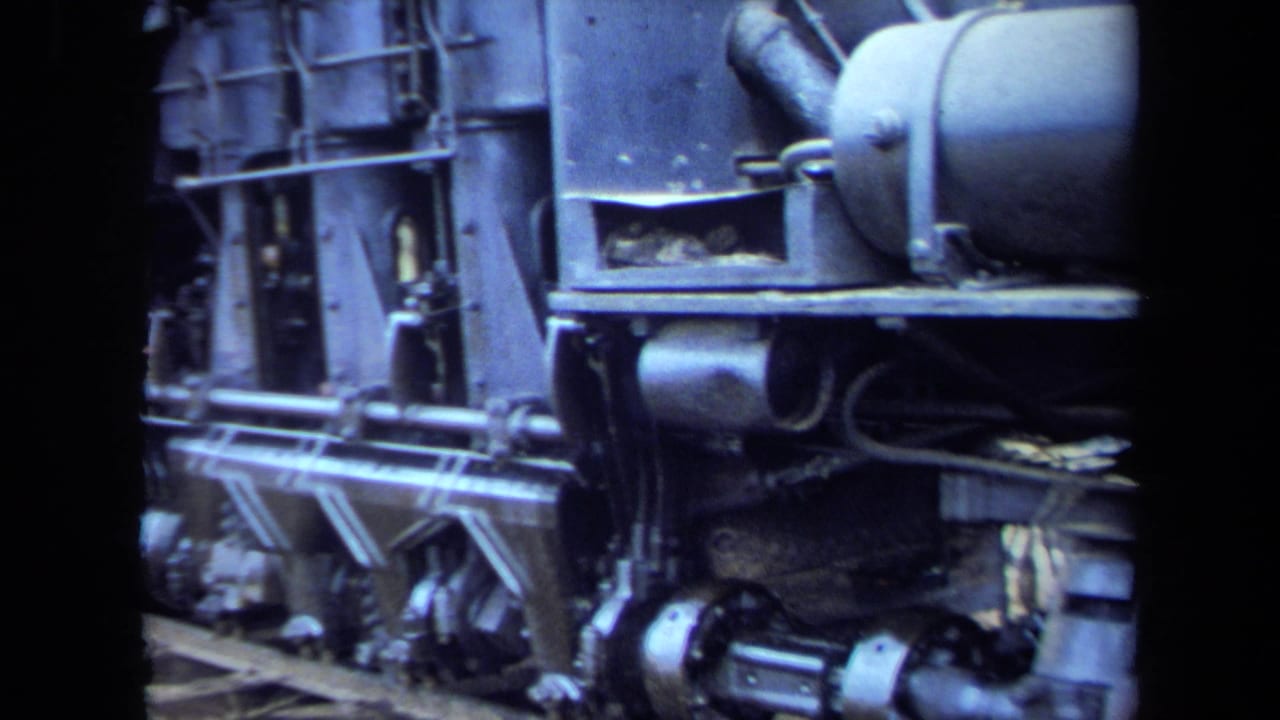 Close-up of a steam locomotive undercarriage with rods, wheels, and side panels.