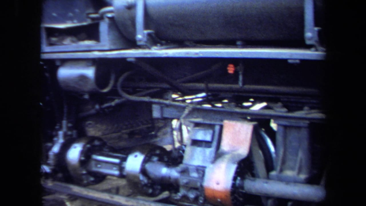 Tight 1970 8mm California view of a steam locomotive wheel assembly, axle, rods, springs, and lower body hardware.