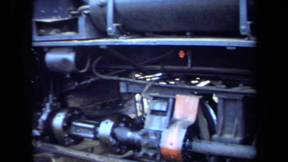 Tight 1970 8mm California view of a steam locomotive wheel assembly, axle, rods, springs, and lower body hardware.