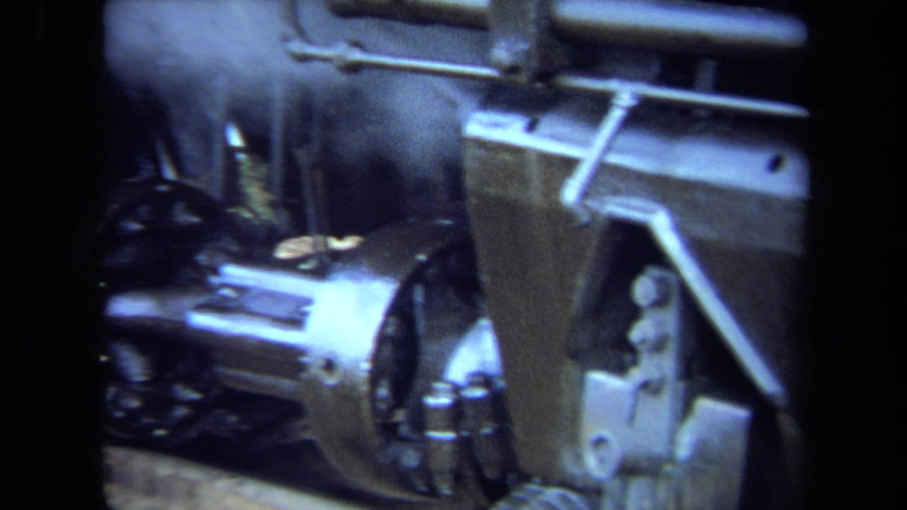 1970 California 8mm frame showing close mechanical detail on a steam locomotive, including wheel, piston housing, rods, and metal bodywork.