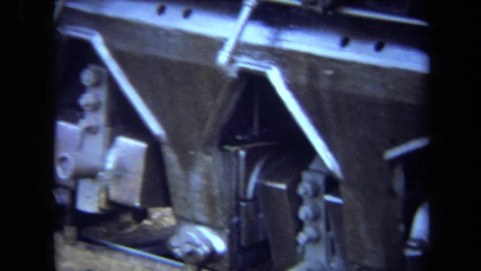 Close 8mm view of steam locomotive bodywork and mechanical fittings, with angled bracing, bolts, and dark painted metal surfaces.
