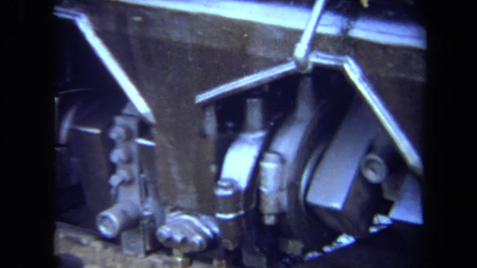 8mm close-up of a steam locomotive's lower side, showing rods, fittings, wheel-edge forms, and heavy metal components.