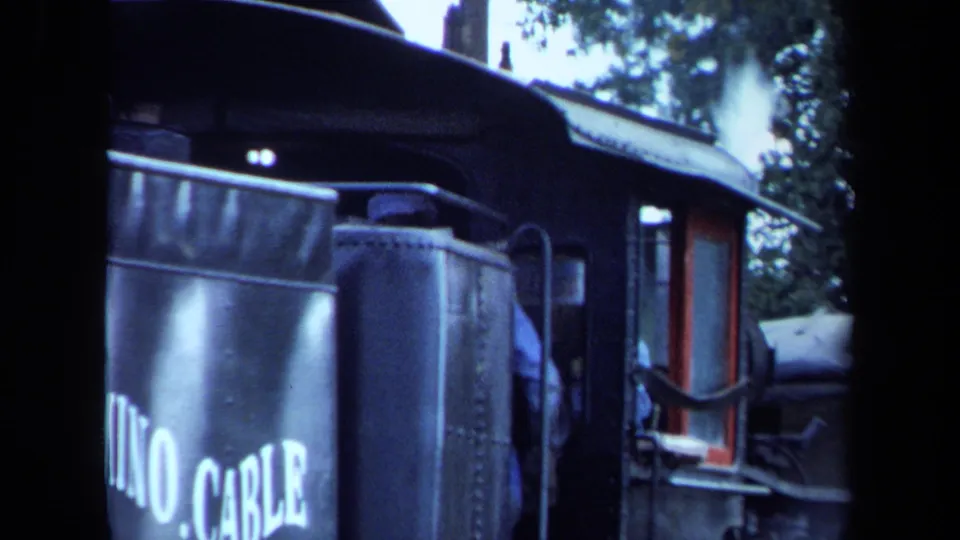 1970 California home-movie frame showing the side of the black locomotive with large white lettering and a partial cab view.