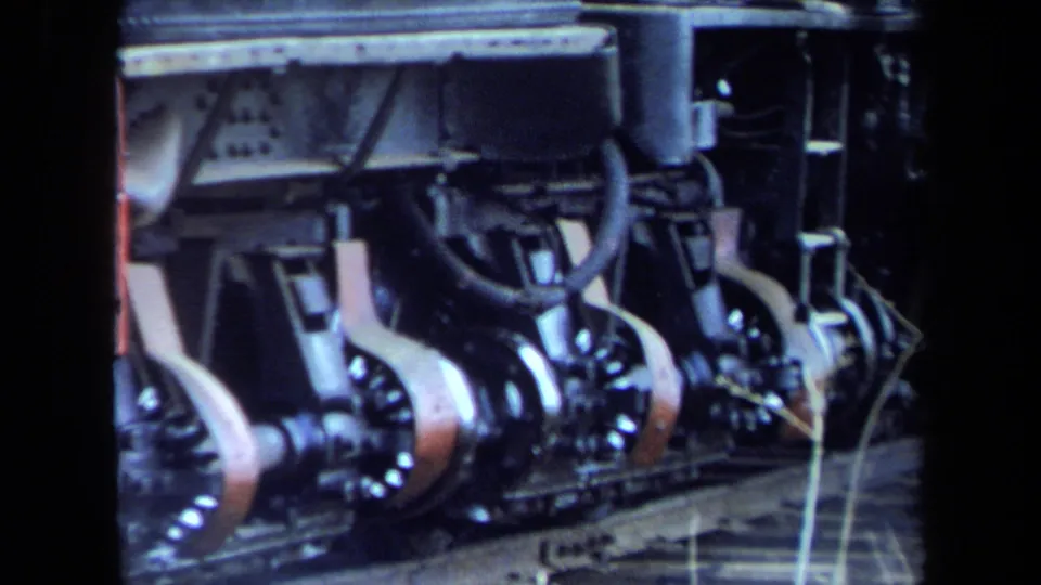 Detailed 8mm close-up of the steam locomotive wheel assembly and connecting rods, with the train body above the track.