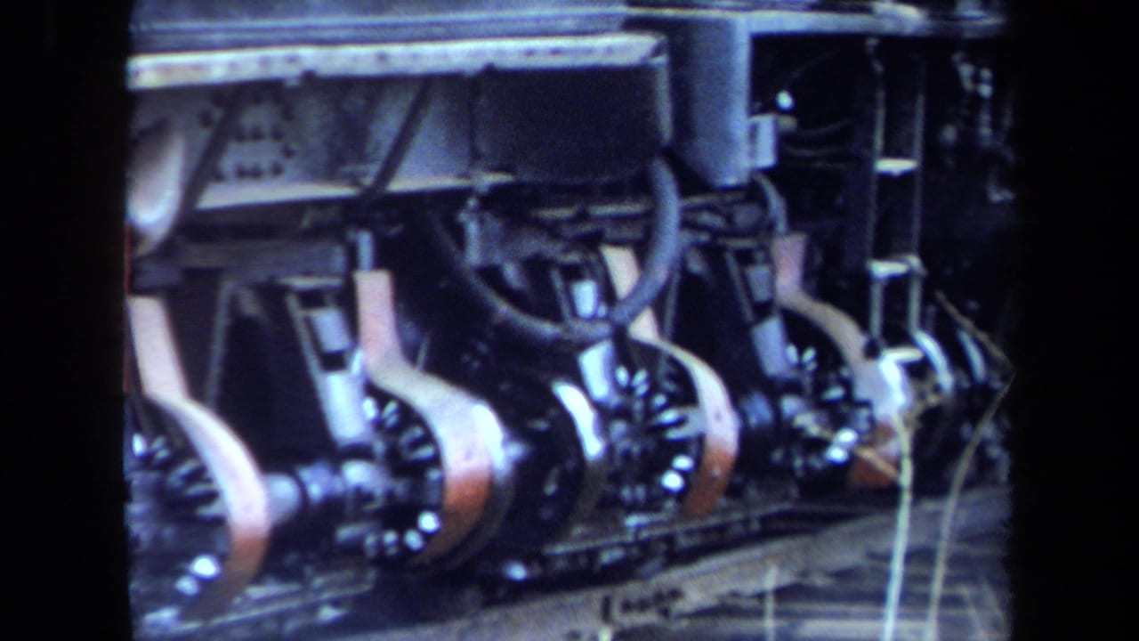 1970 California 8mm frame showing steam locomotive rods, wheels, piping, and red metalwork in close-up.