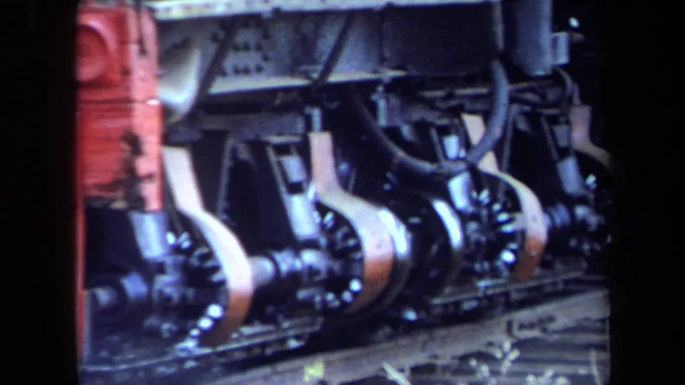 Close 8mm view of steam locomotive running gear, with black wheels, pale rods, and red painted hardware.