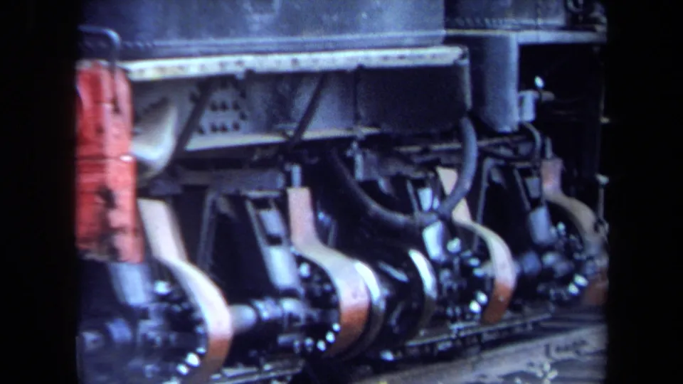 1970 home-movie frame of locomotive rods and wheels, with the contact-sheet border and soft color visible.