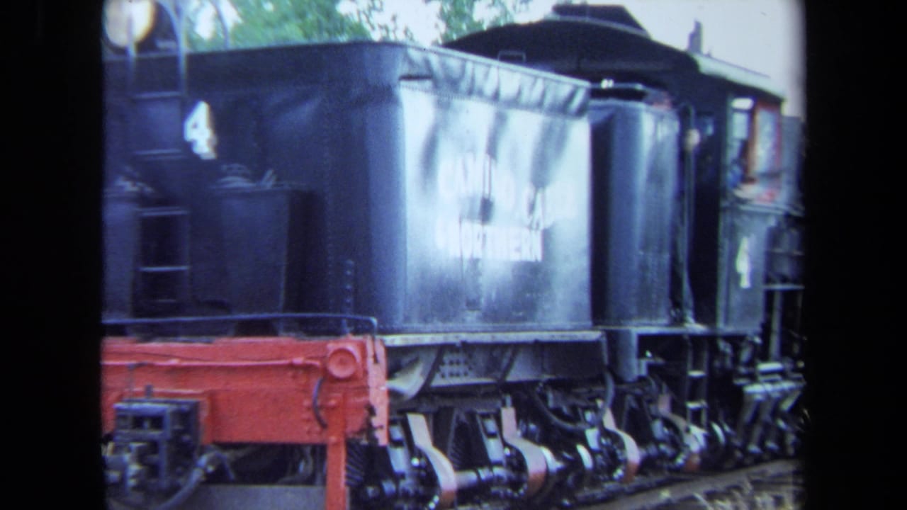 1970 California 8mm frame showing a black steam locomotive numbered 4 moving past the camera, with red lower hardware and soft trees behind it.