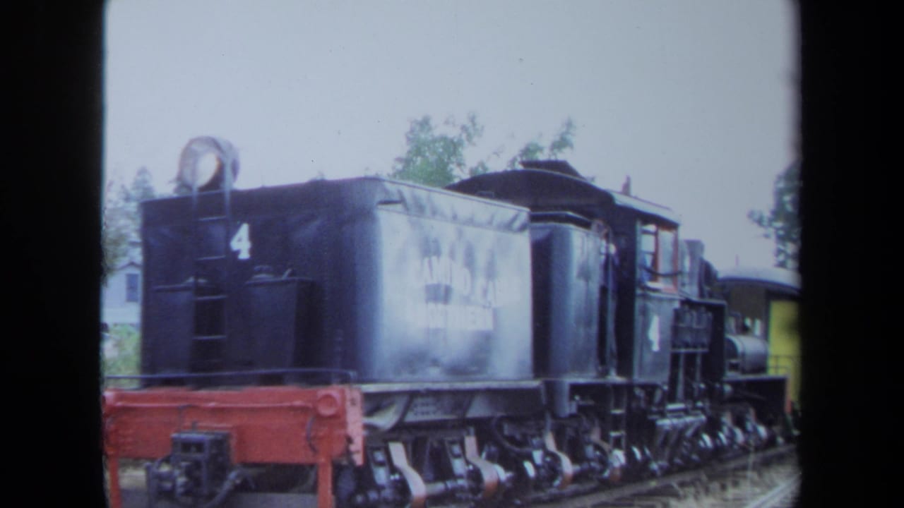 1970 California 8mm frame of locomotive number 4 on a railroad track, with white lettering on the tender and a yellow car in the background.