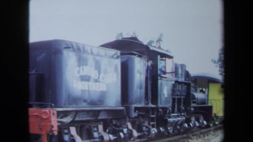 1970 California 8mm frame with the tender side of a black steam locomotive close to camera, showing partial white lettering and mechanical running gear.