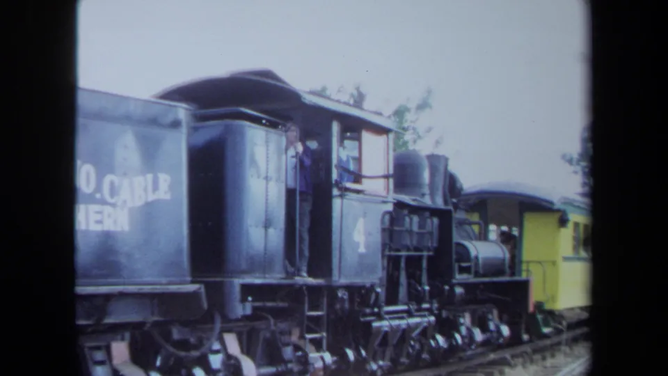1970 California 8mm frame showing the locomotive cab area with number 4, a yellow railcar behind, and a person briefly visible at the window.