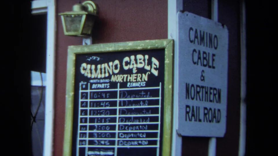 Close 8mm view of Camino Cable & Northern Railroad signage, including a chalkboard timetable and a painted wall sign by a doorway.