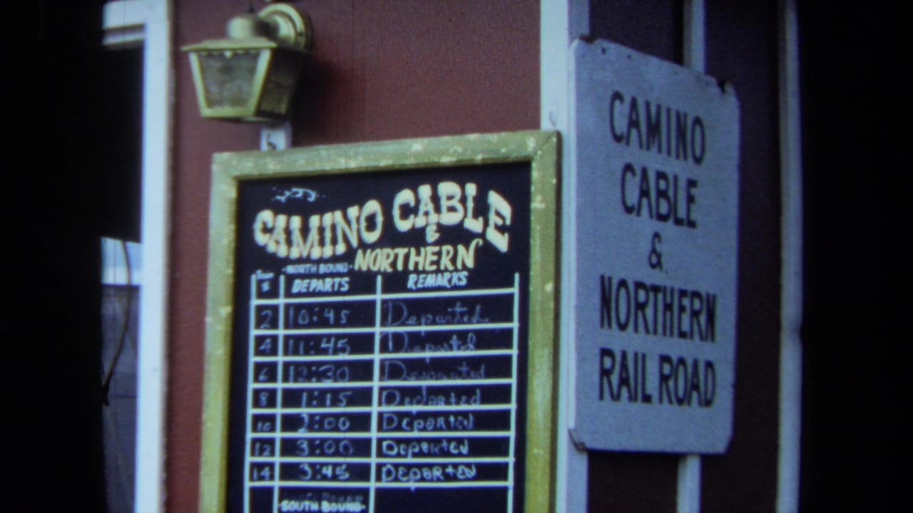 1970 California 8mm frame showing Camino Cable and Northern Railroad signage, a posted departure board, red siding, and a wall lantern.