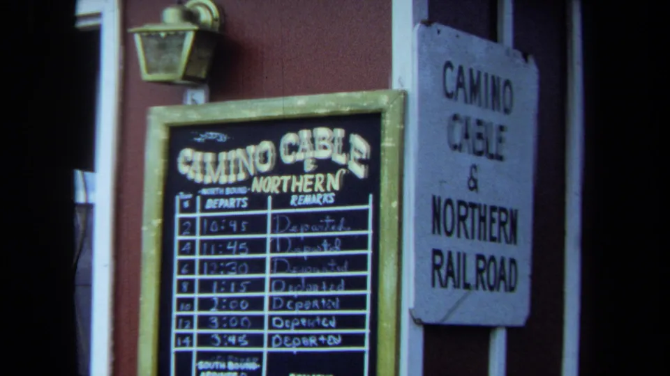 1970 California 8mm frame with a close view of Camino Cable and Northern Railroad station-style signage and a handwritten schedule board.