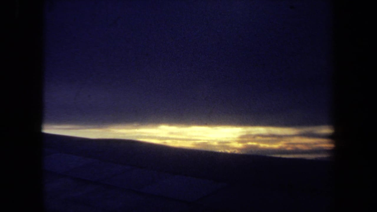 1970 California 8mm frame showing a yellow horizon beneath dark clouds, viewed through shadowed edges over possible water or a deck.