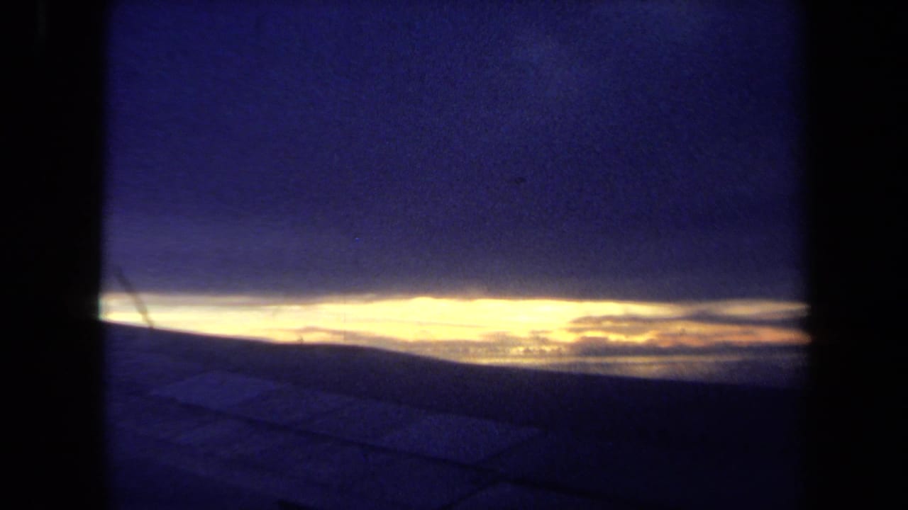 1970 California 8mm view of a bright horizon line under deep blue clouds, with dark framing suggesting a window or film gate.
