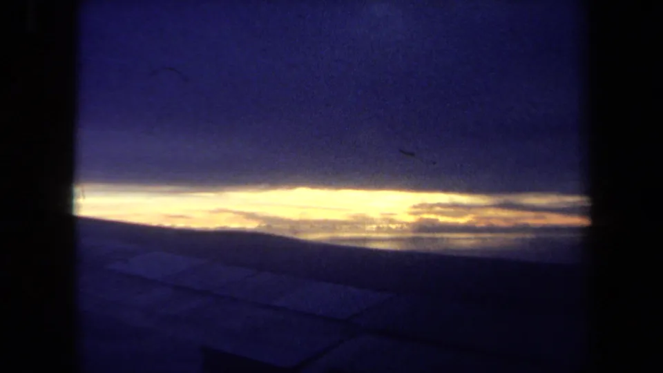 1970 California 8mm frame with sunset or sunrise light stretching across clouds above a dark possible water or deck foreground.