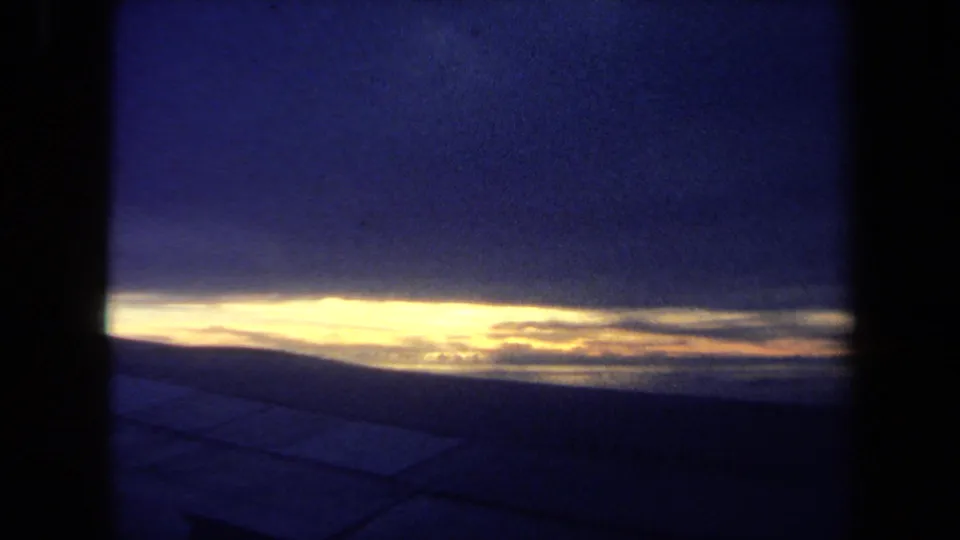 1970 California 8mm shot of a narrow sunset or sunrise band over a dark foreground, framed by heavy shadowed edges.