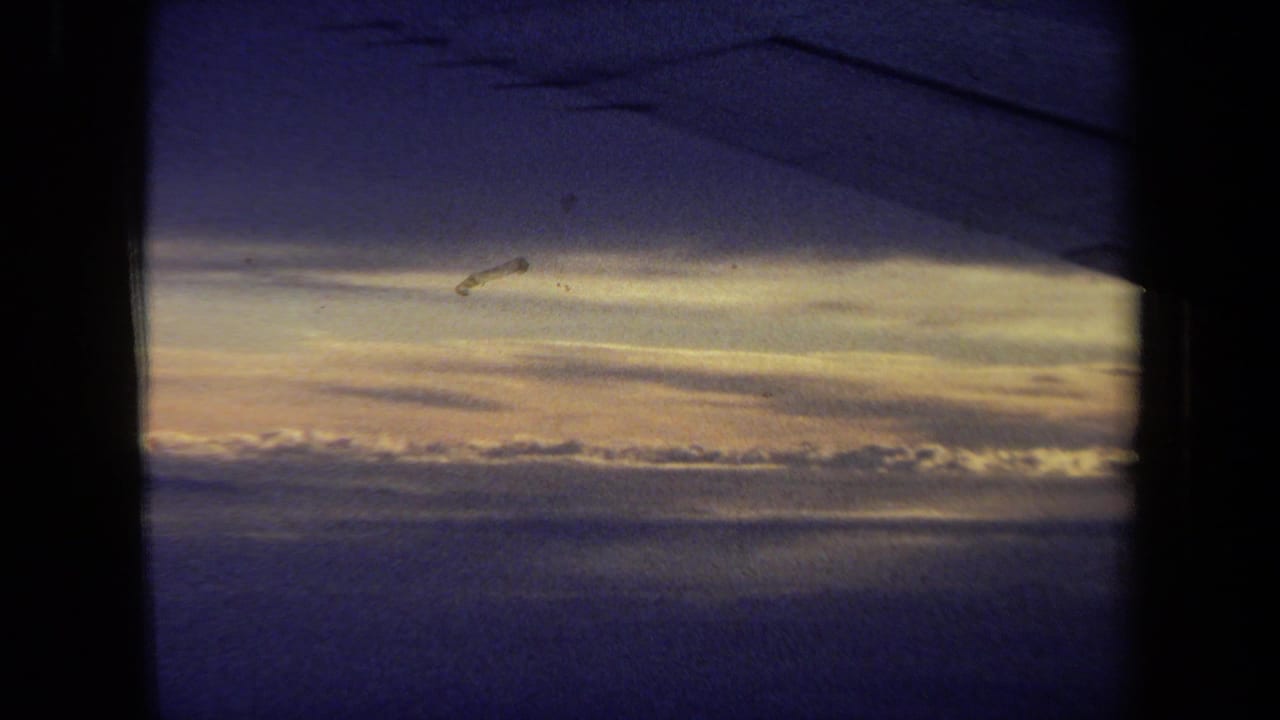 1970 California 8mm passenger-window view with a dark wing silhouette, golden cloud bands, and blue upper sky.