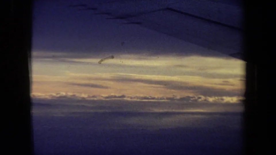 1970 California 8mm passenger-window view with a dark wing silhouette, golden cloud bands, and blue upper sky.