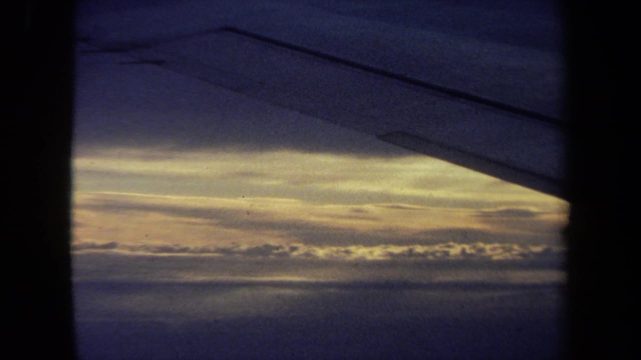 Airplane wing edge seen through a dark window frame over layered clouds.