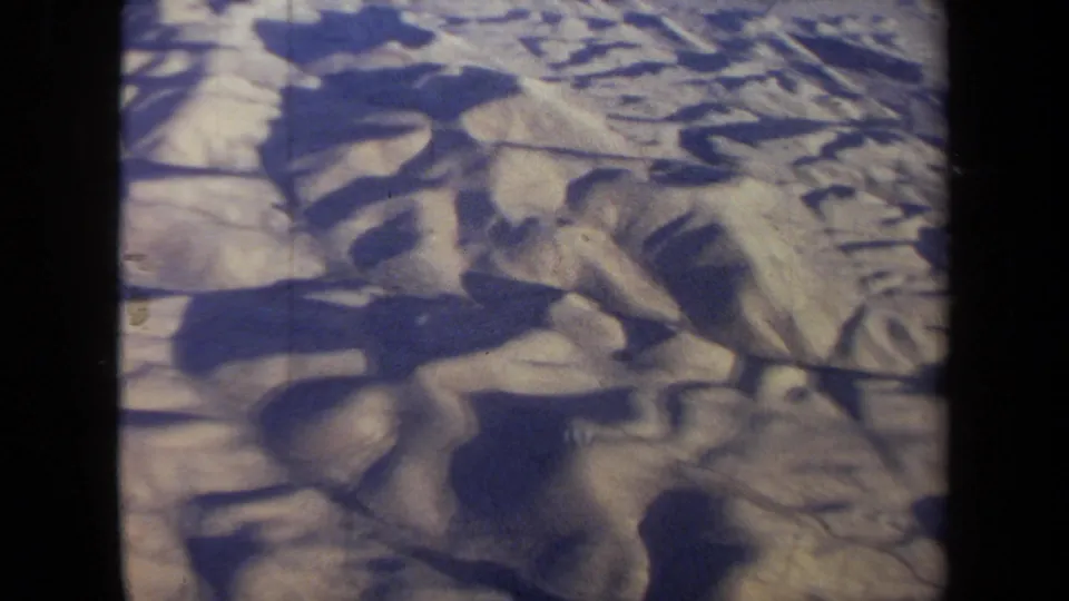 1970 California 8mm aerial frame with pale ridged ground, blue shadows, and dark passenger-window borders.