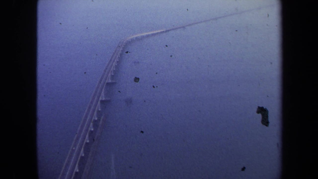 A bridge or causeway crosses water in a hazy aerial view with film dust and dark borders.
